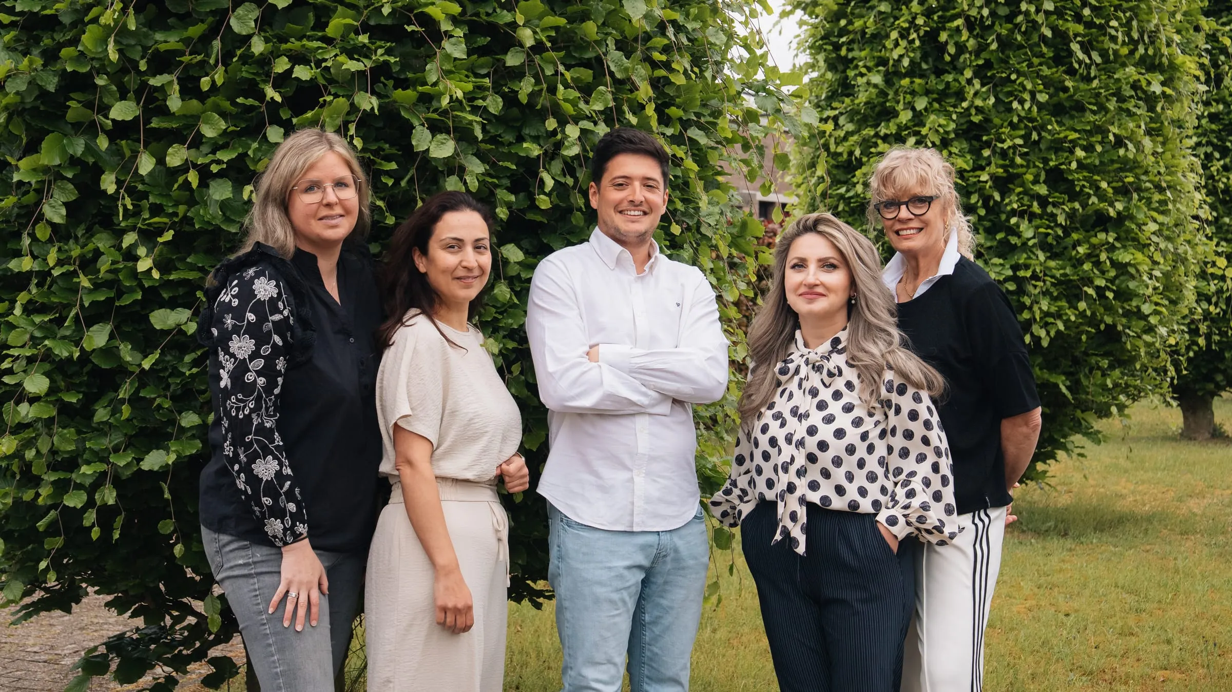 Het team van Mondzorg Schaijk lacht samen bij de beukenhaag naast de praktijk